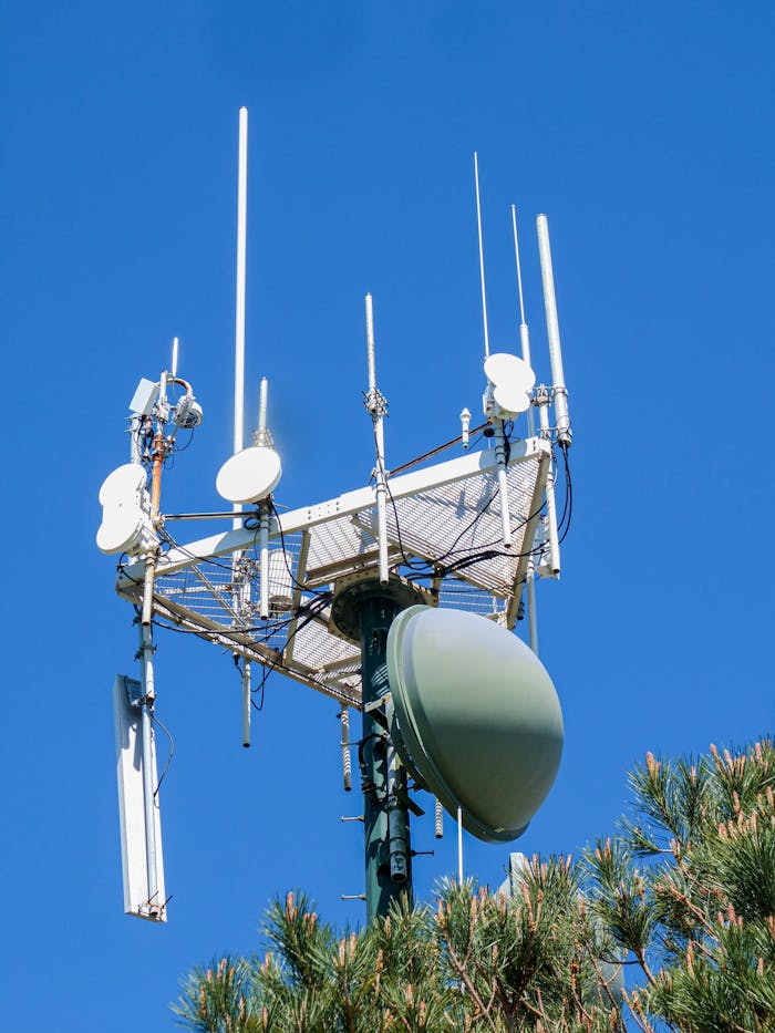 A modern antenna tower with various antennae and dishes, set against a vibrant clear blue sky.